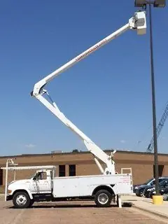 Baker Electric bucket truck with the boom raised to a pole, the kind of overhead work that pairs with a well job's underground run