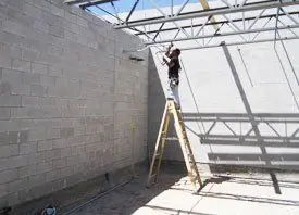 Electrician on a ladder against a block wall under steel joists